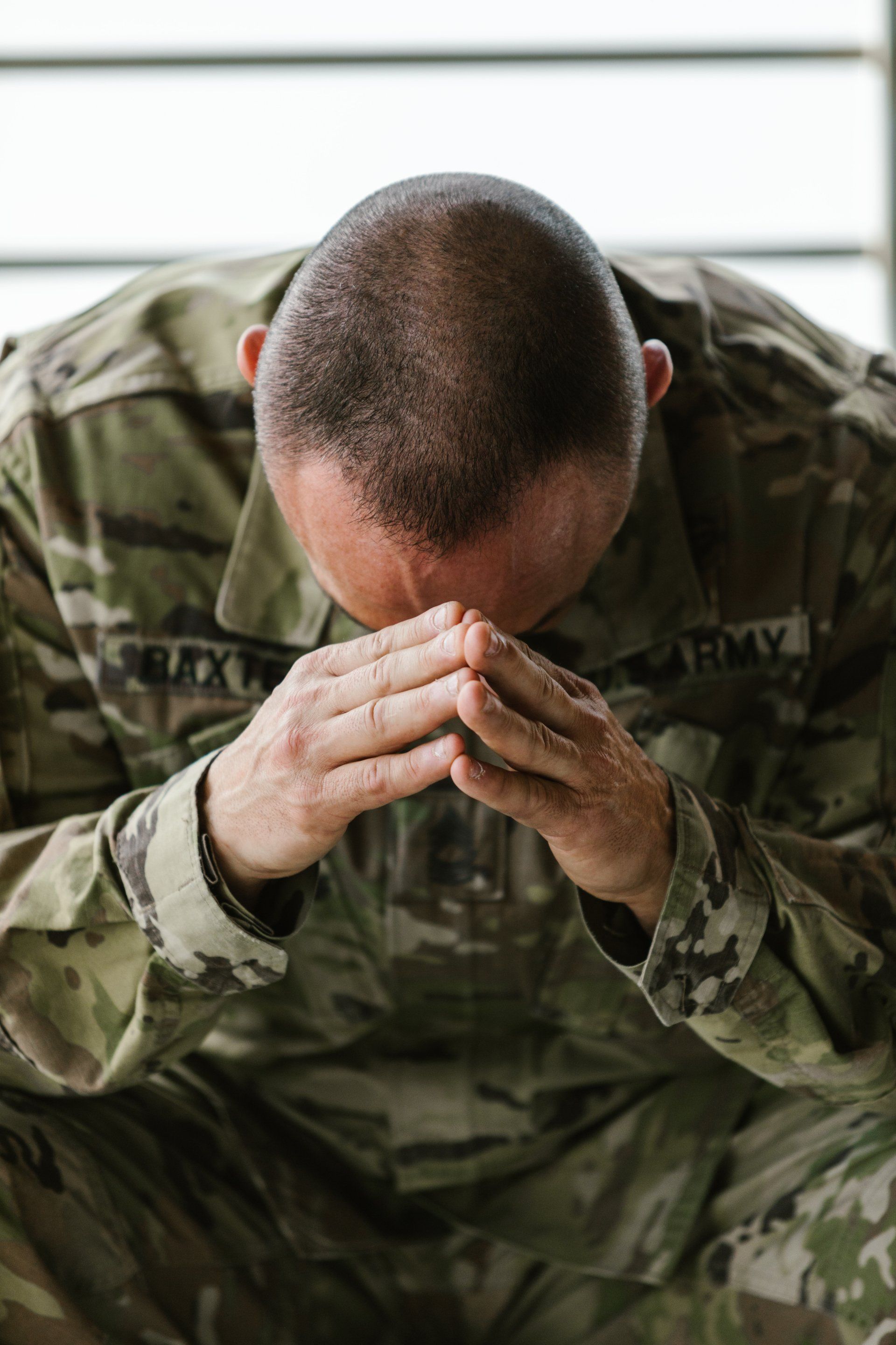 Soldier in camouflage uniform sitting with head bowed and hands clasped in prayer