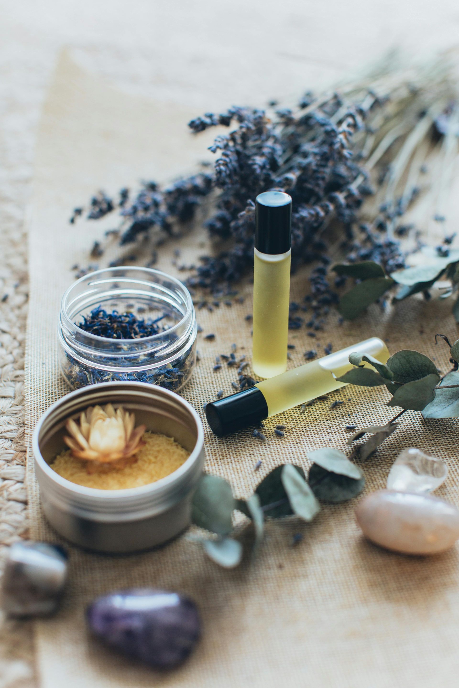 Aromatherapy items on burlap: essential oil bottles, dried lavender, candles, and crystals.